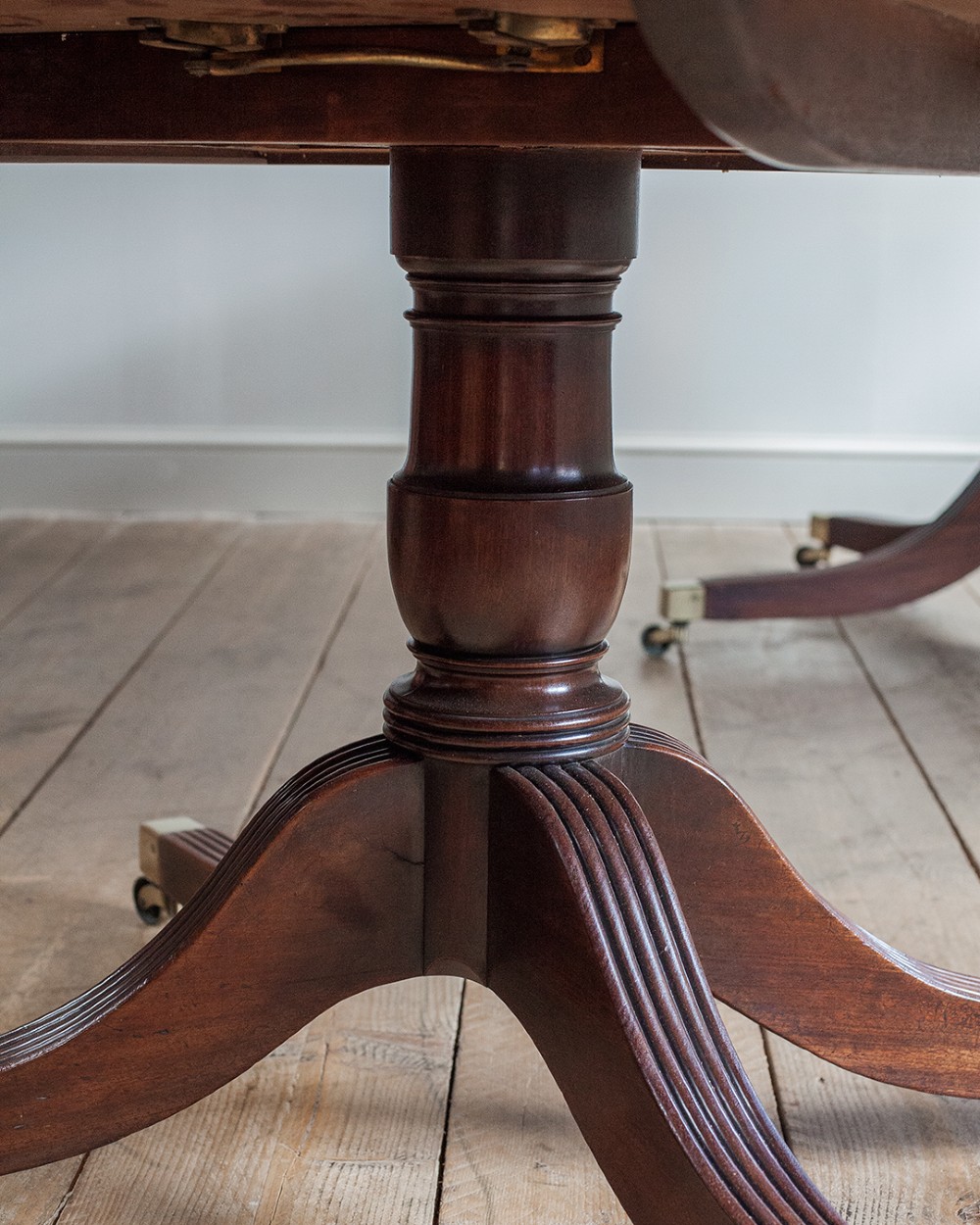 A Regency mahogany extending twin pedestal dining table with rounded corners, reeded splayed legs, and brass caps with castors. View V