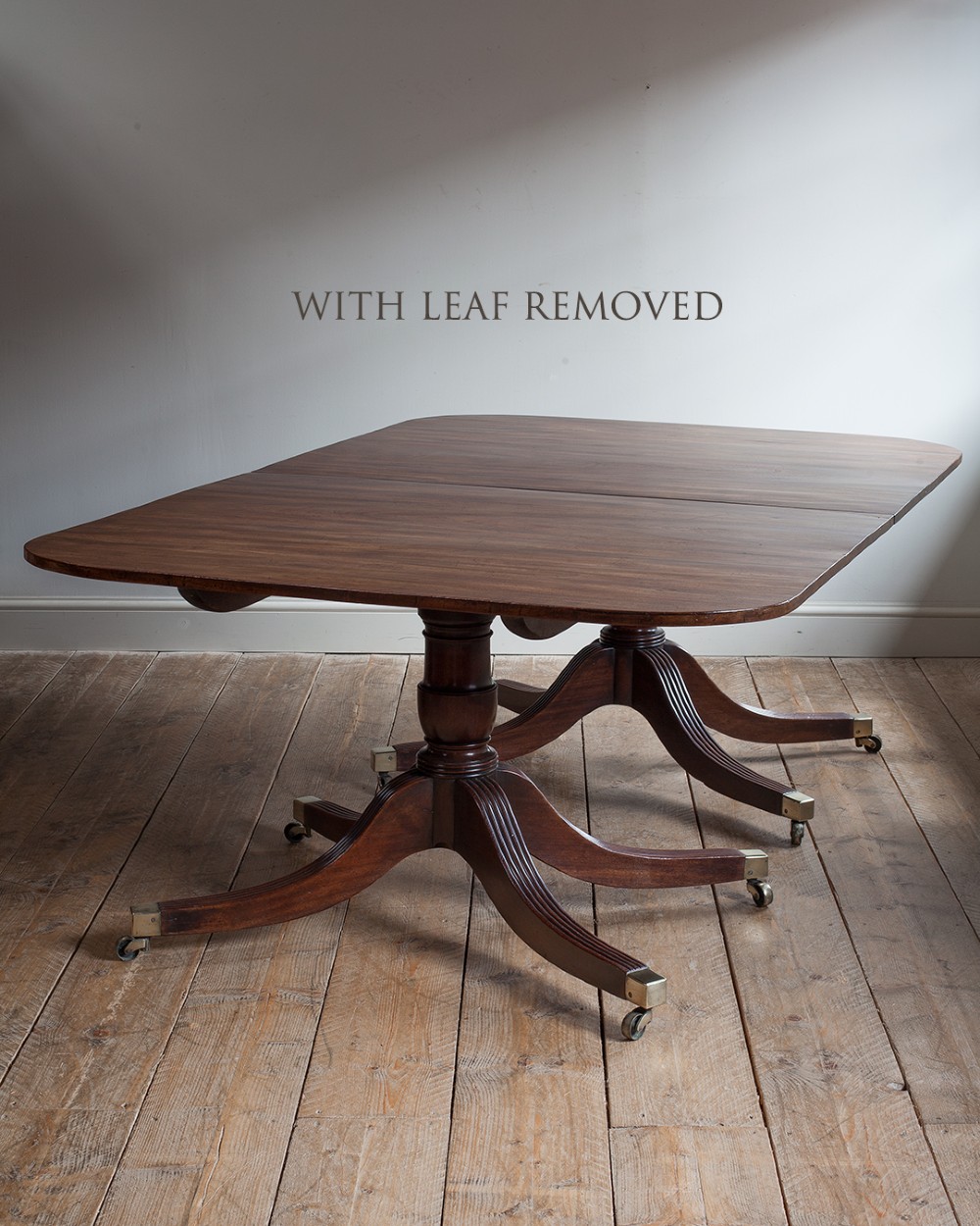 A Regency mahogany extending twin pedestal dining table with rounded corners, reeded splayed legs, and brass caps with castors. View VII