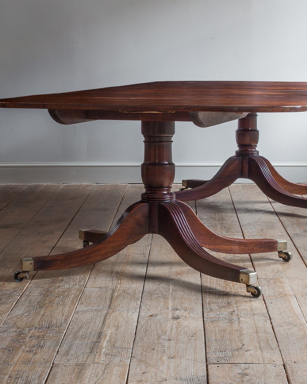 A Regency mahogany extending twin pedestal dining table with rounded corners, reeded splayed legs, and brass caps with castors. View IX