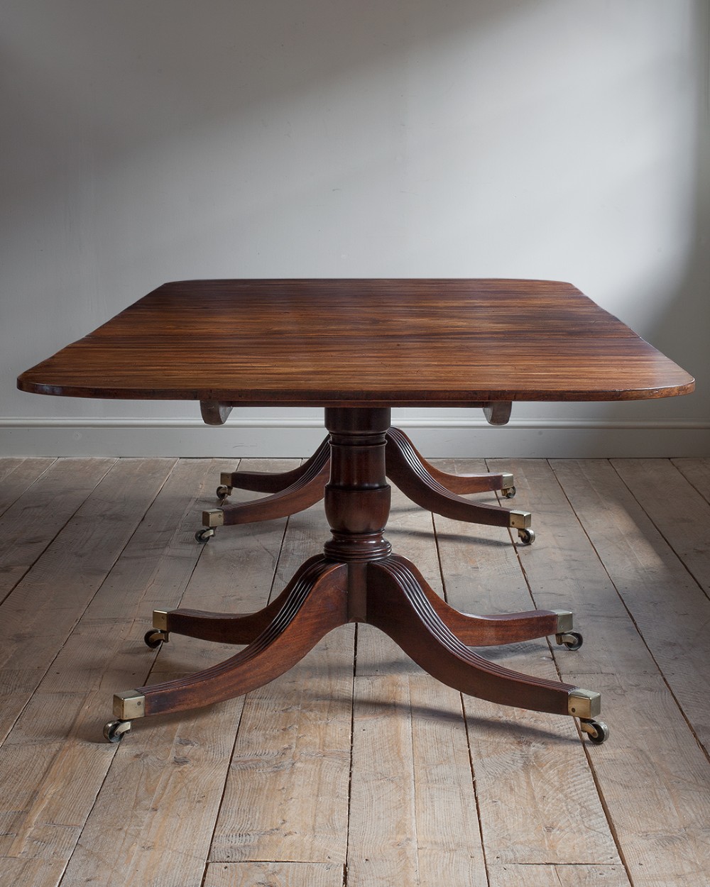 A Regency mahogany extending twin pedestal dining table with rounded corners, reeded splayed legs, and brass caps with castors. View XI