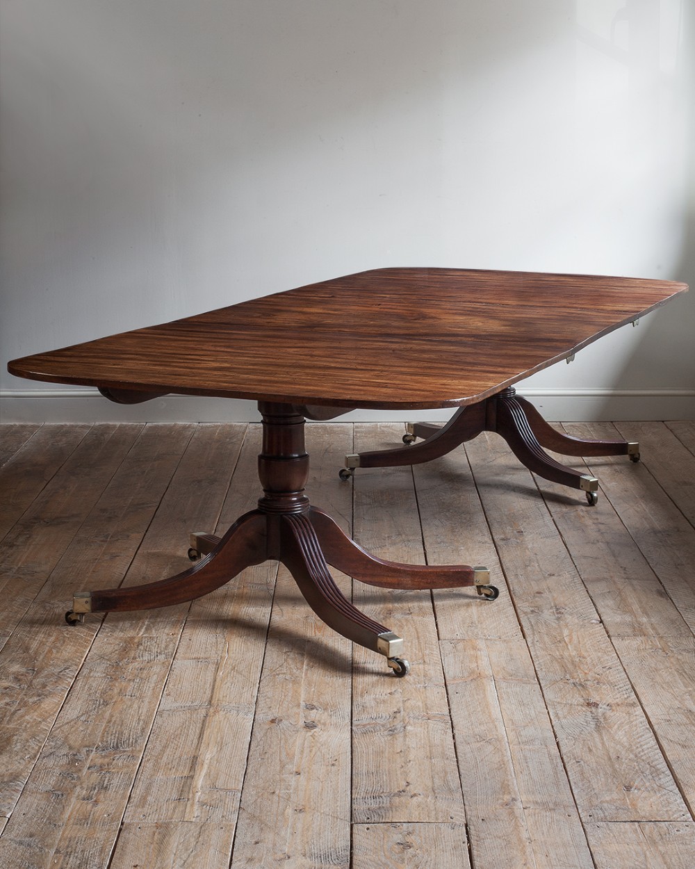 A Regency mahogany extending twin pedestal dining table with rounded corners, reeded splayed legs, and brass caps with castors.
