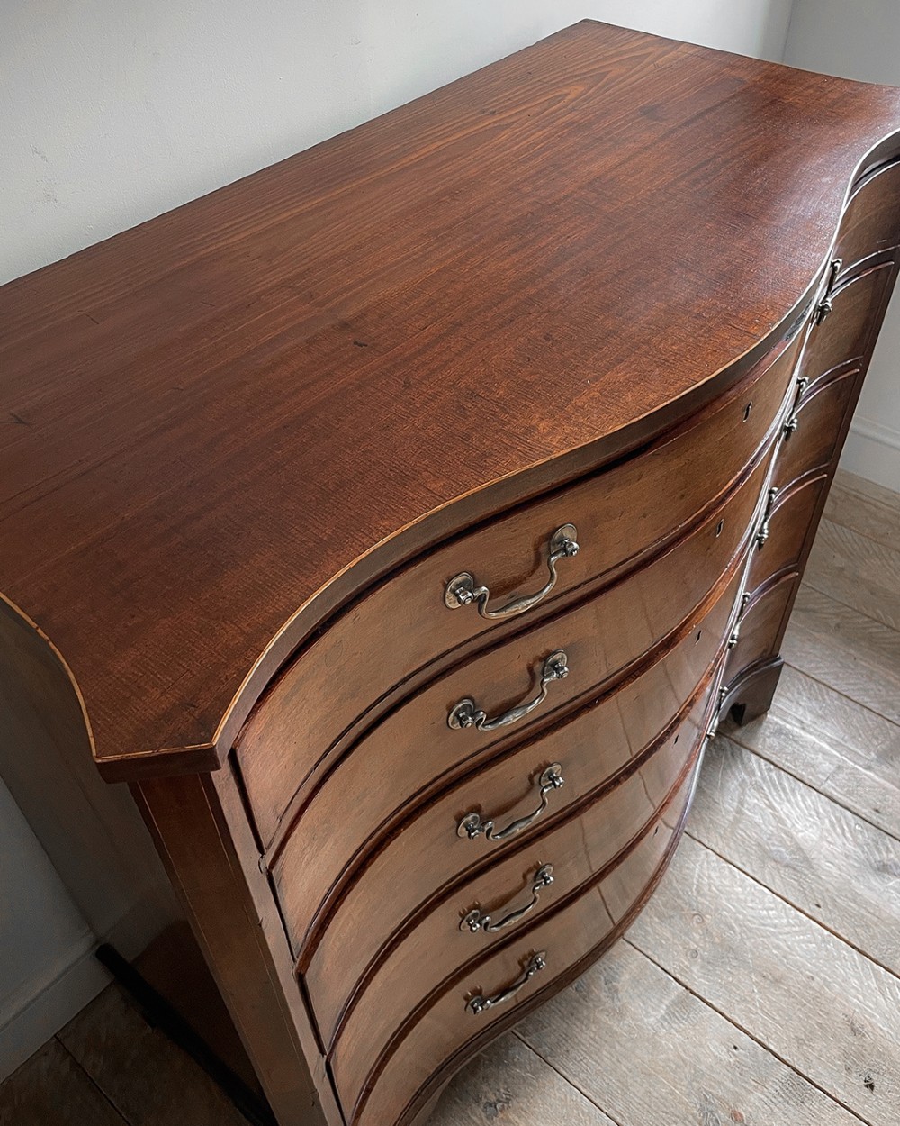 A George III mahogany chest of drawers featuring a serpentine front, five graduated drawers with brass swan-neck handles, and shaped bracket feet. View II