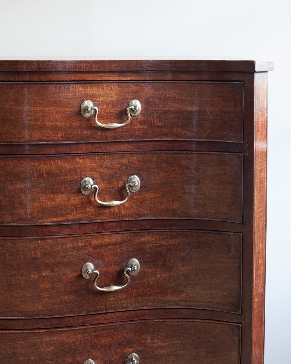 A George III mahogany chest of drawers featuring a serpentine front, five graduated drawers with brass swan-neck handles, and shaped bracket feet. View V