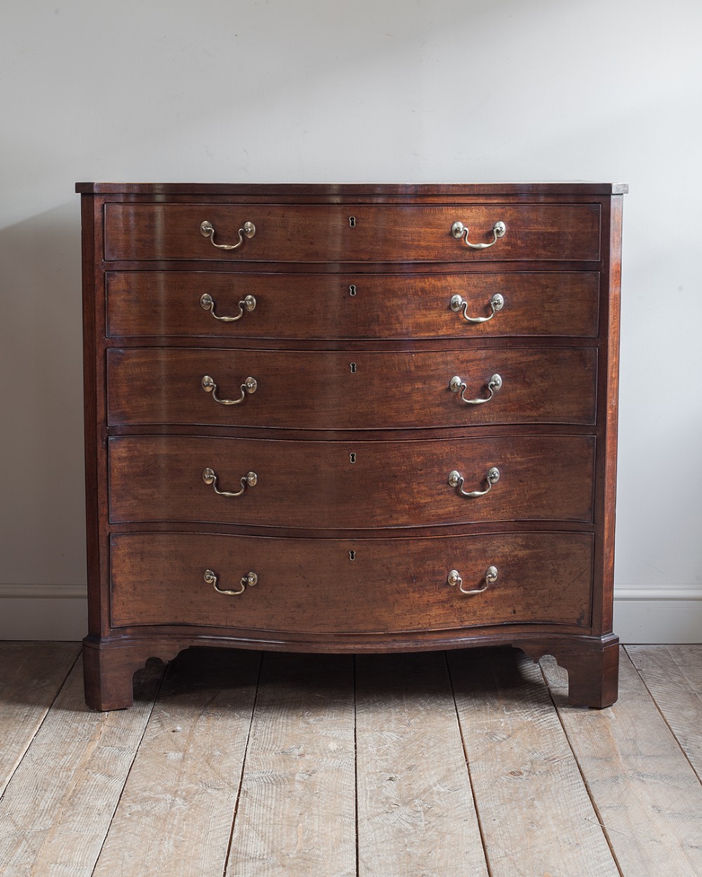 A George III mahogany chest of drawers featuring a serpentine front, five graduated drawers with brass swan-neck handles, and shaped bracket feet. View VI