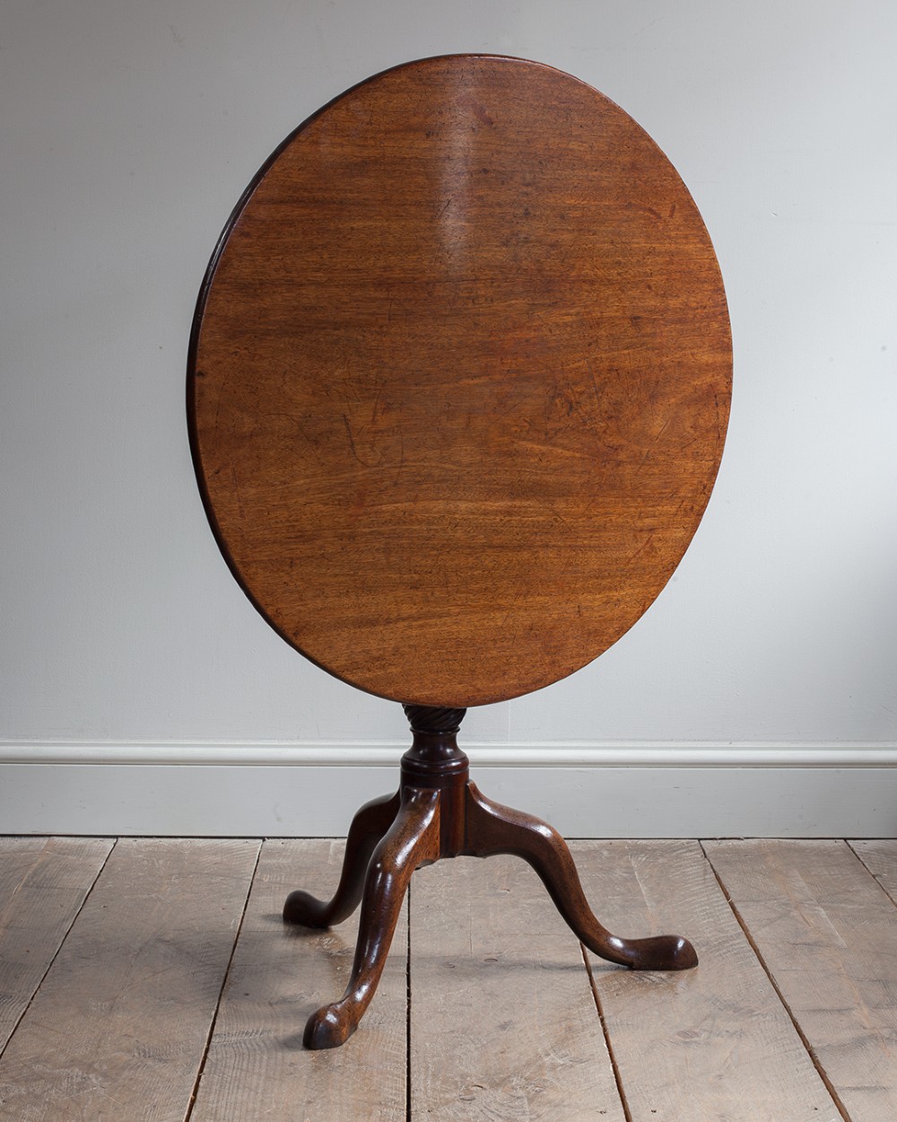A George III mahogany tripod table featuring a circular top supported by a turned pedestal column with spiral carving and three cabriole legs. View IX