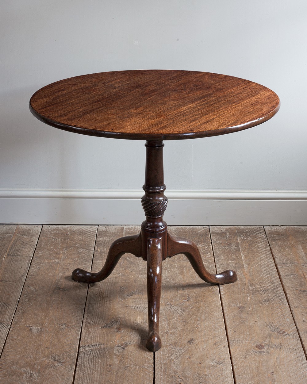 A George III mahogany tripod table featuring a circular top supported by a turned pedestal column with spiral carving and three cabriole legs.