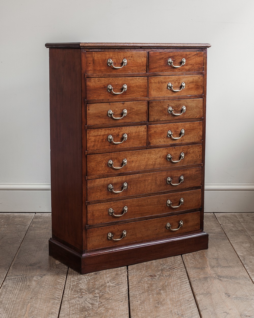 A tall 19th-century mahogany bank of drawers featuring eight tiers of small and wide drawers with brass handles, resting on a solid plinth base.