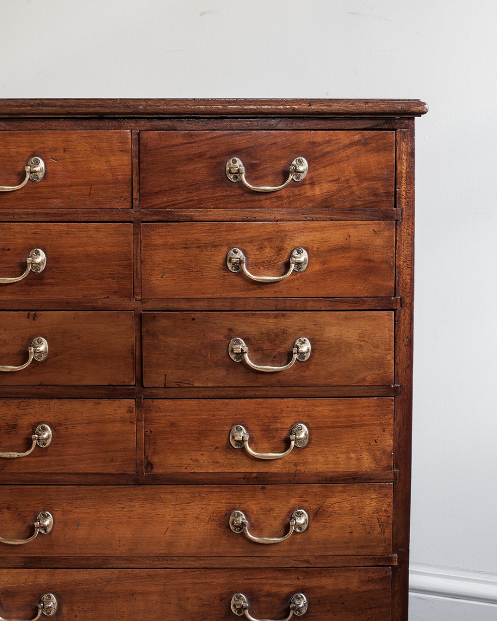 A tall 19th-century mahogany bank of drawers featuring eight tiers of small and wide drawers with brass handles, resting on a solid plinth base. View V