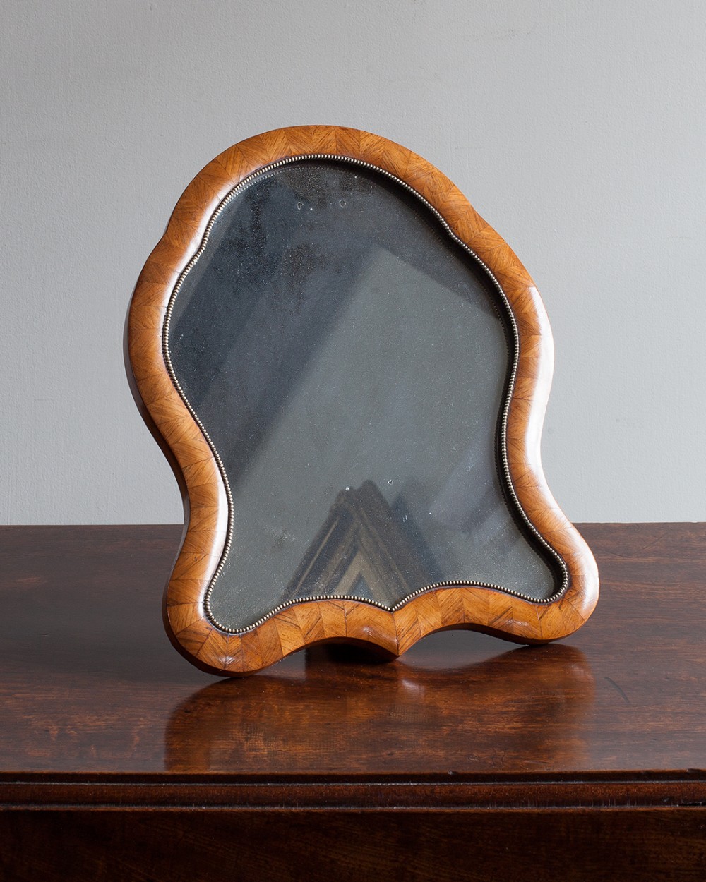 A small 19th-century cartouche-shaped table mirror with herringbone kingwood parquetry veneer and a beaded brass inner trim.