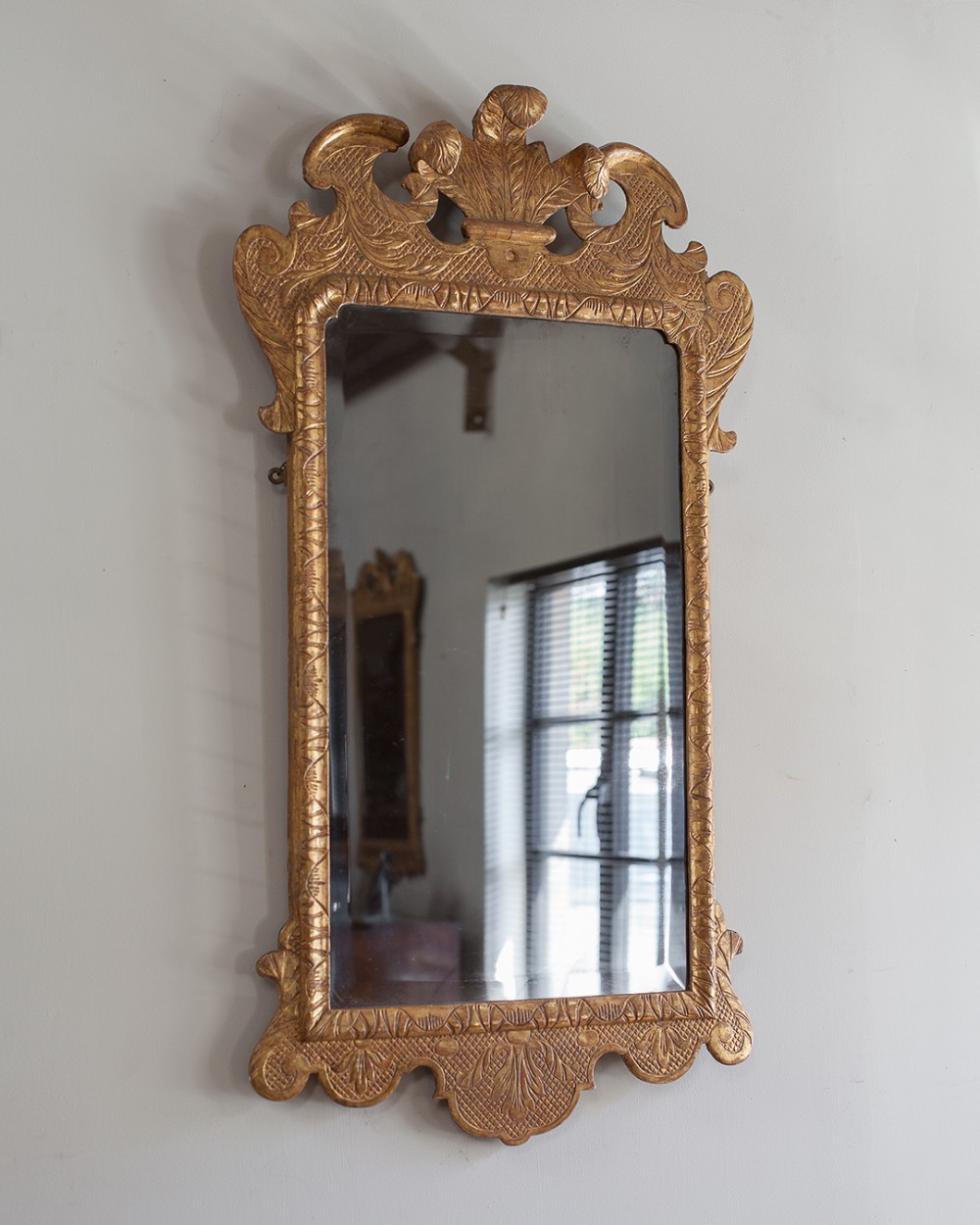 A carved George II giltwood wall mirror featuring an acanthus leaf cresting and intricate low-relief patterned borders.