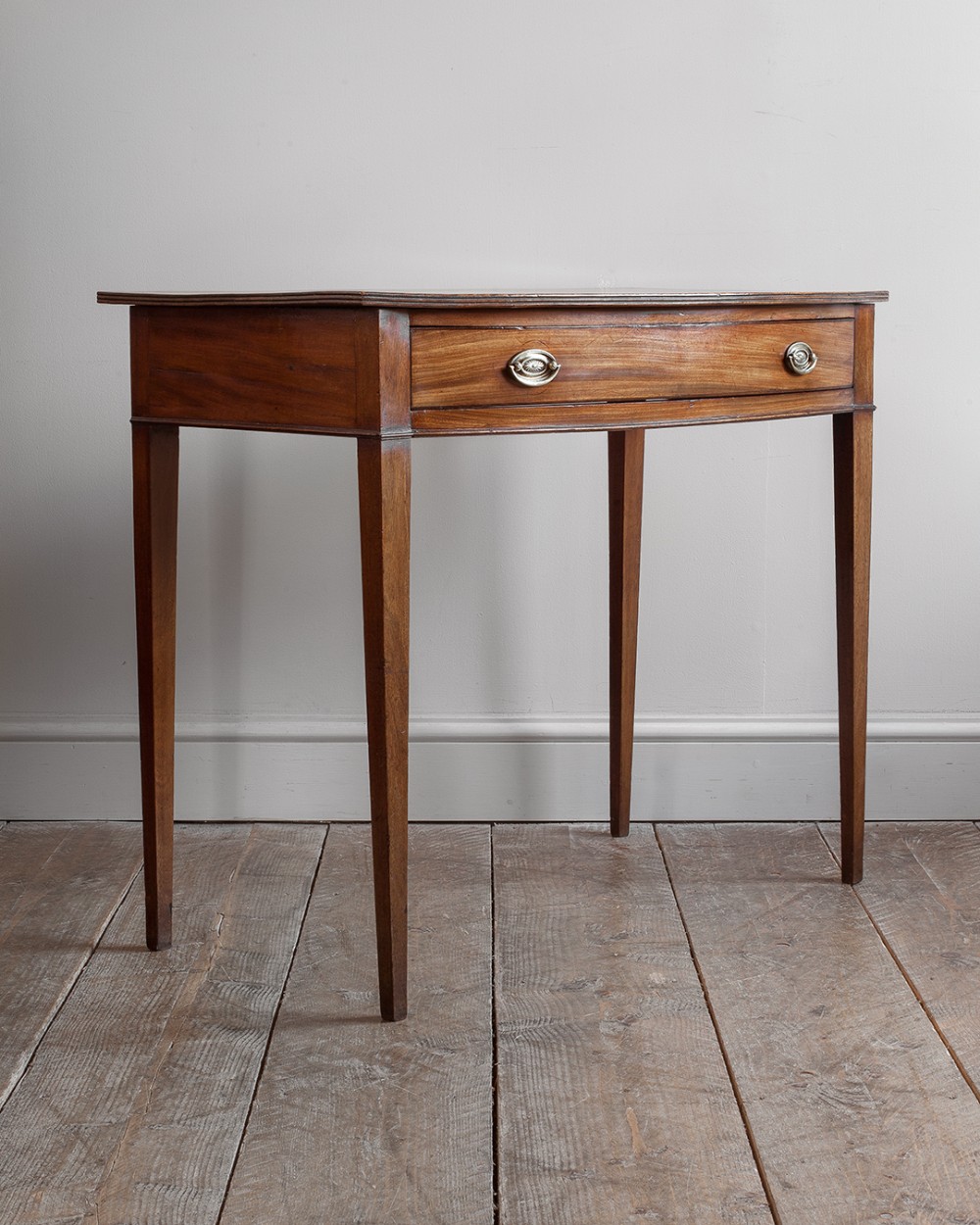 A Georgian mahogany bowfront side table featuring a single curved drawer with oval brass handles and four tapered square legs.