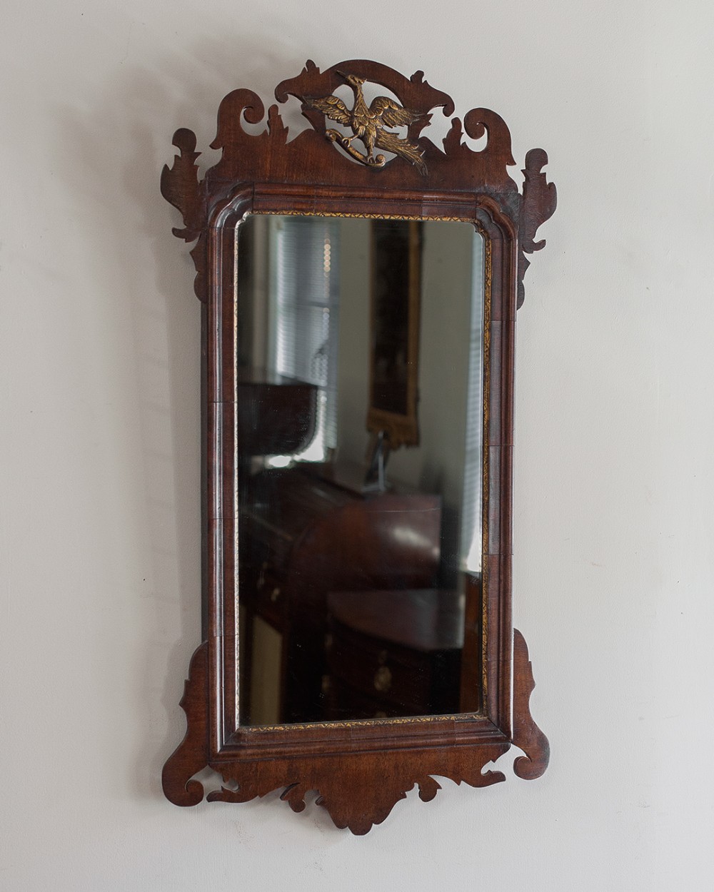 An 18th-century style mahogany fretwork wall mirror featuring a scroll-cut silhouette frame with a central gilded bird cresting.