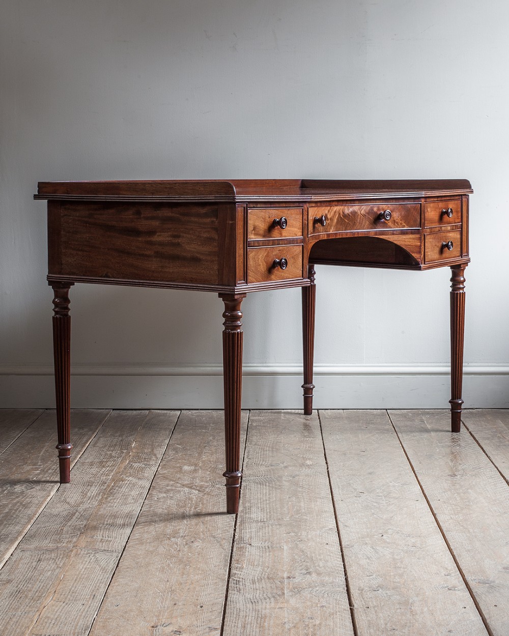 A Regency mahogany dressing table featuring a low gallery border, five drawers with turned wooden handles, a central kneehole, and tapered reeded legs.