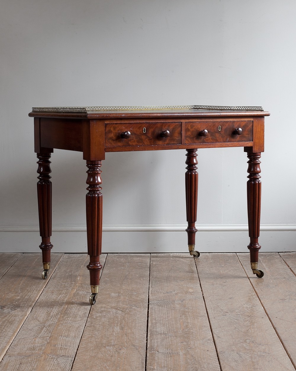 A 19th-century mahogany writing table with two frieze drawers, turned reeded legs, brass castors, and a brass gallery along the back.