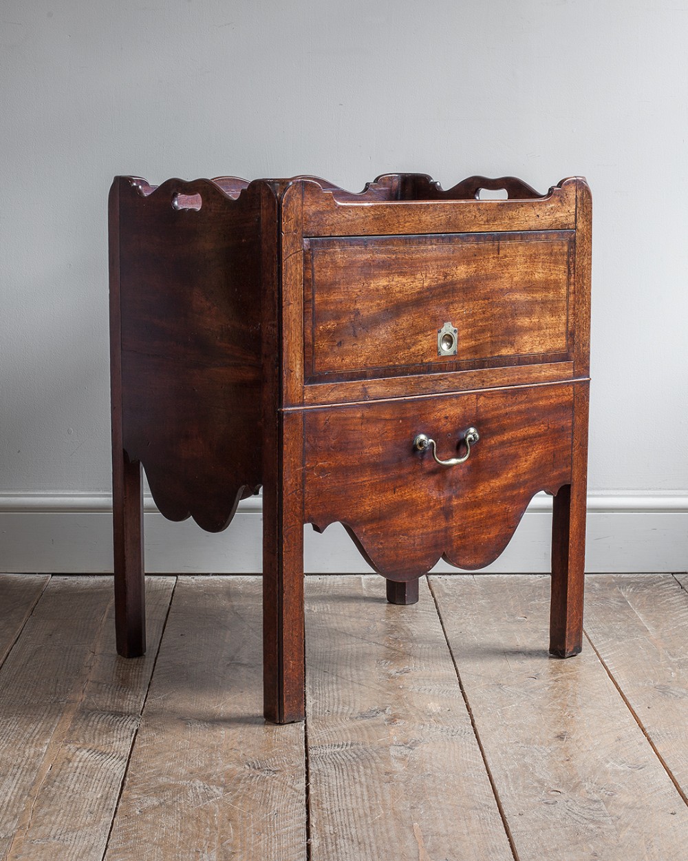 A George III mahogany tray-top nightstand with cut-out gallery handles, a central drawer compartment, and a lower drawer above a shaped apron.