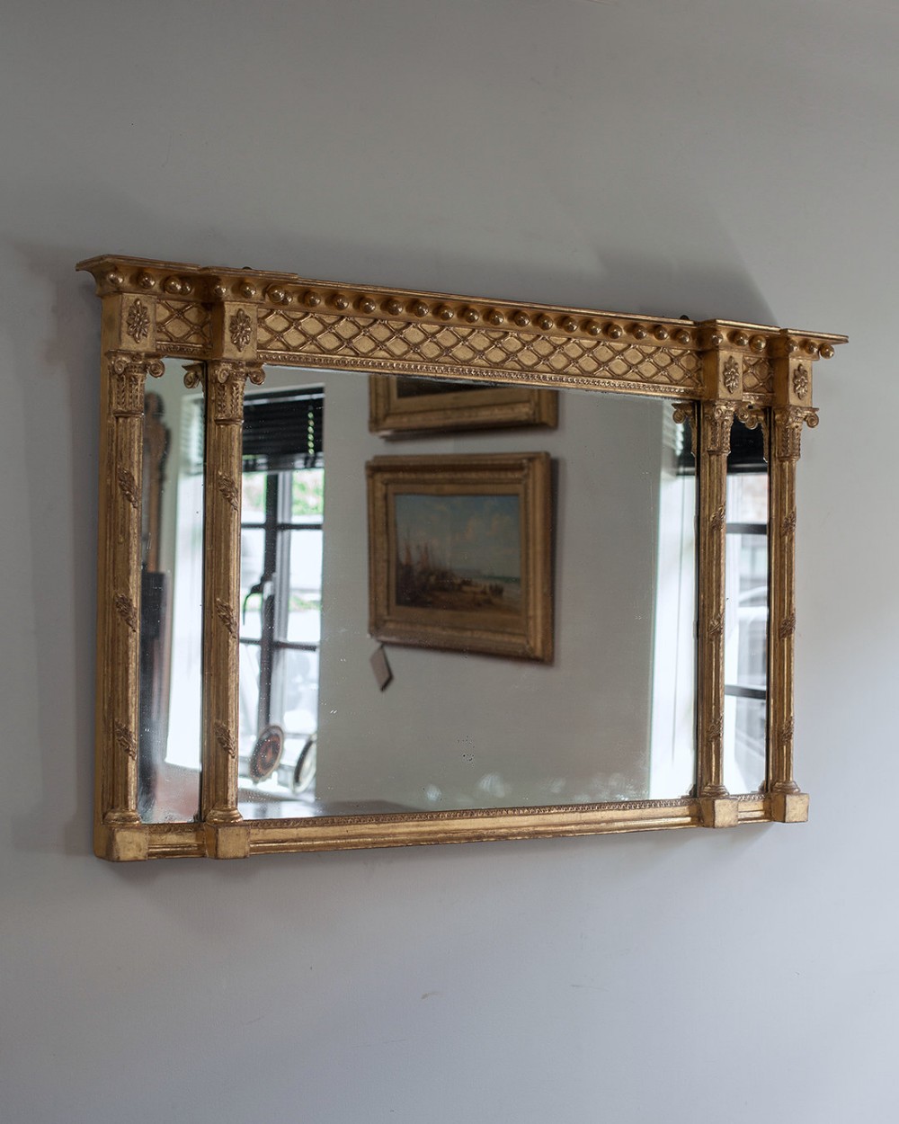 A horizontal Regency giltwood overmantel mirror featuring three glass plates, twin cluster side columns with capitals, a lattice frieze, and a ball-moulded breakfront cornice.