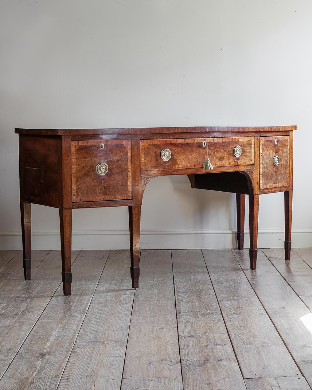 A Georgian mahogany bowfront sideboard featuring a central drawer flanked by deep side cupboards, tapered square legs, and octagonal brass handles.
