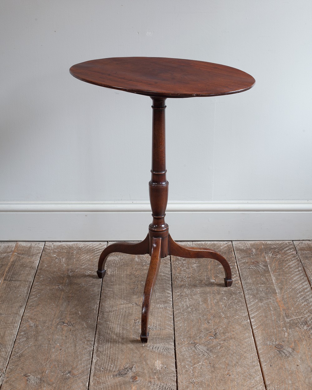 A George III mahogany occasional table featuring an oval surface set upon a turned pedestal column and three downswept tripod legs.