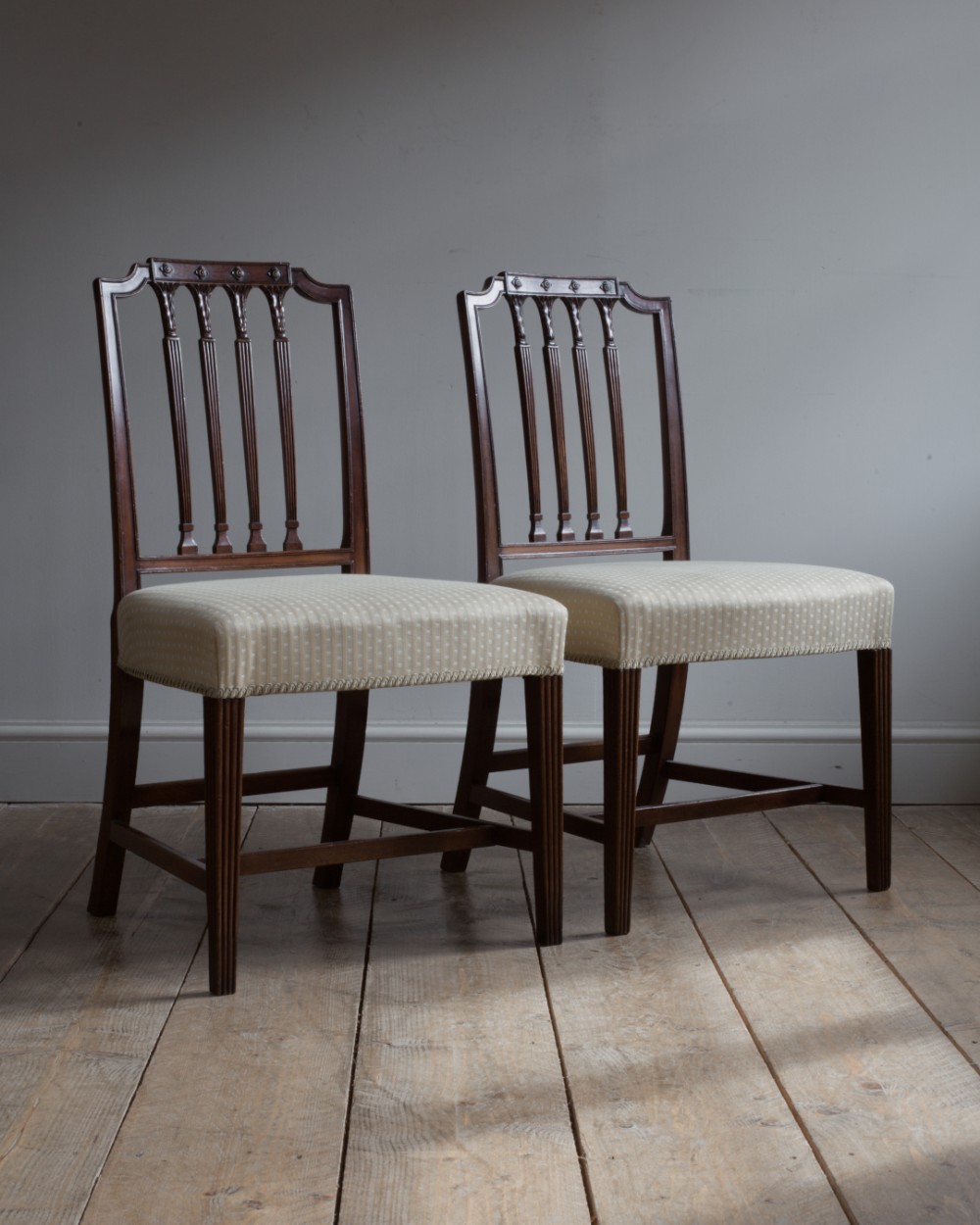 A pair of George III mahogany dining chairs with carved fluted splats and light cream patterned upholstered seats.