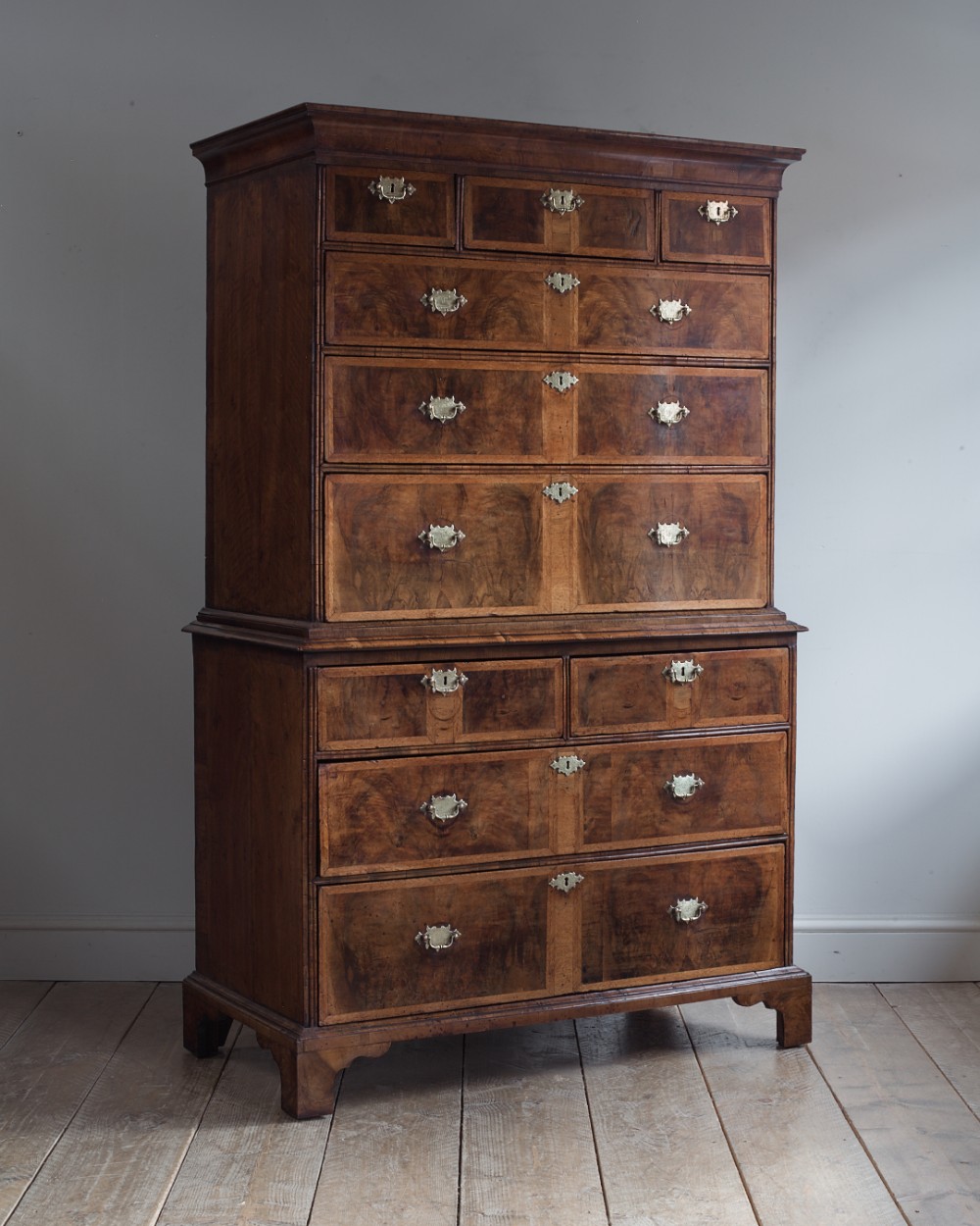 A George II walnut chest-on-chest featuring an upper section with drawers over a lower base section, fitted with brass drop handles and resting on bracket feet.