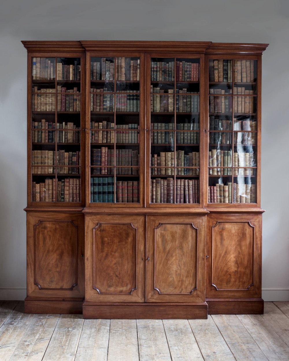 A large George III mahogany breakfront library bookcase featuring four glazed upper doors above four panelled timber doors.