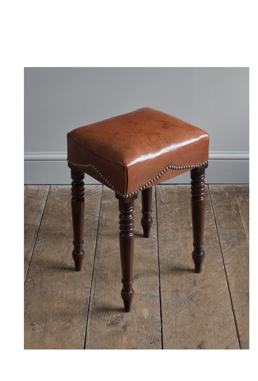 A dark mahogany Regency stool with turned legs and a square top upholstered in tan leather with brass stud detail. View II