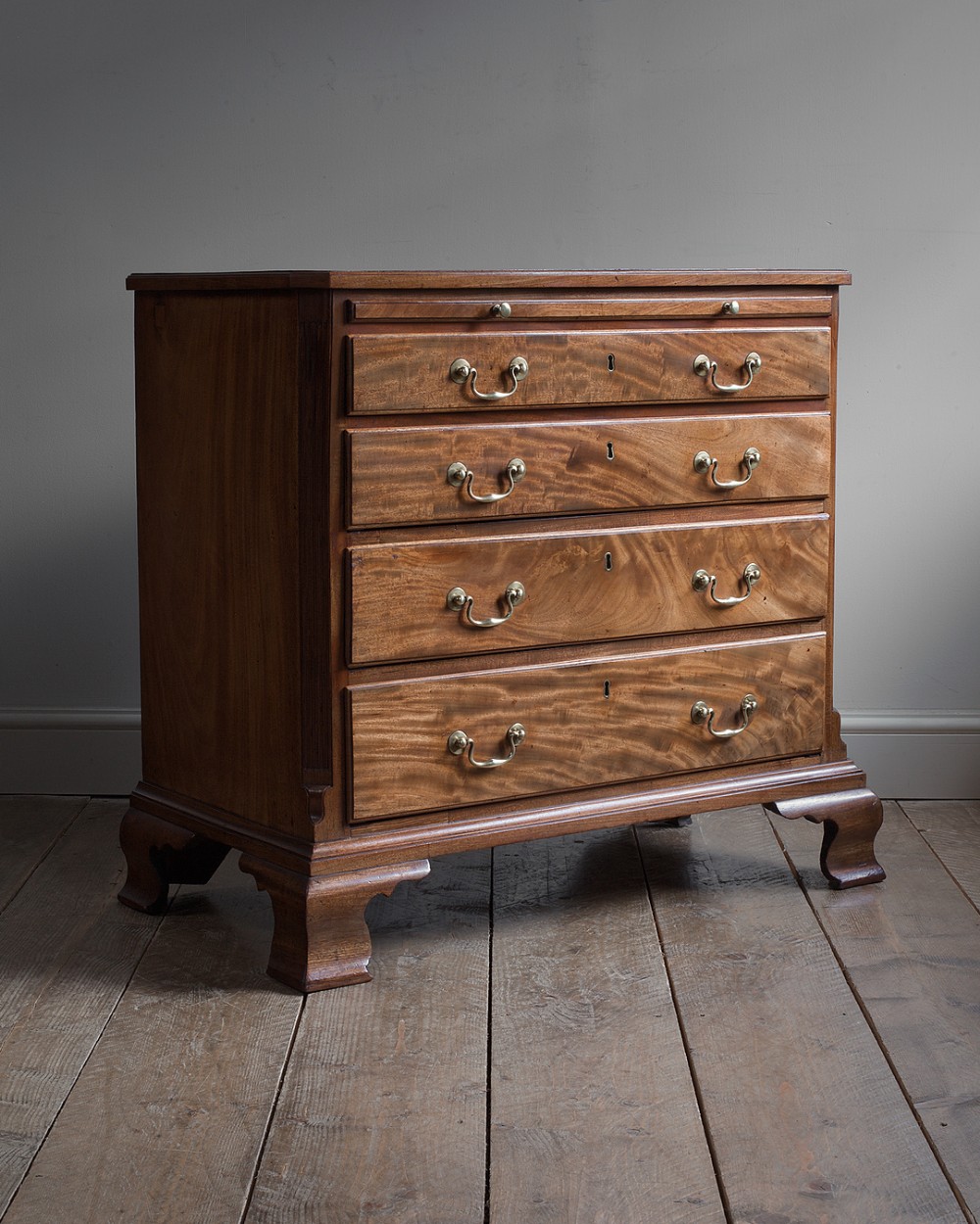 An 18th-century George III mahogany chest of four graduated drawers featuring brass swan-neck handles, a pull-out brushing slide, fluted pilasters, and shaped bracket feet.