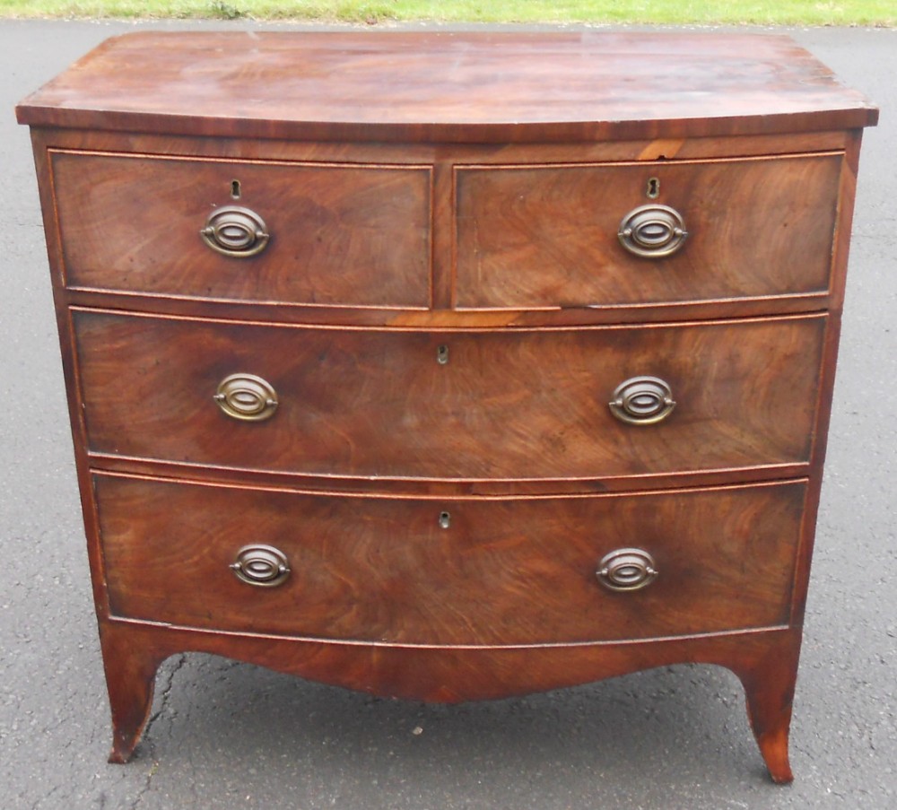 A Georgian mahogany bowfront chest of drawers featuring two short drawers over two long drawers with oval brass handles and splay feet.