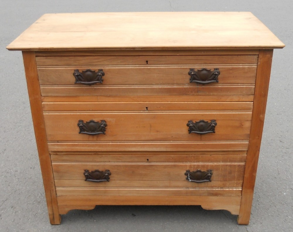 An Edwardian satin walnut chest of drawers featuring three graduated drawers with decorative metal drop handles and linear reeded moulding.