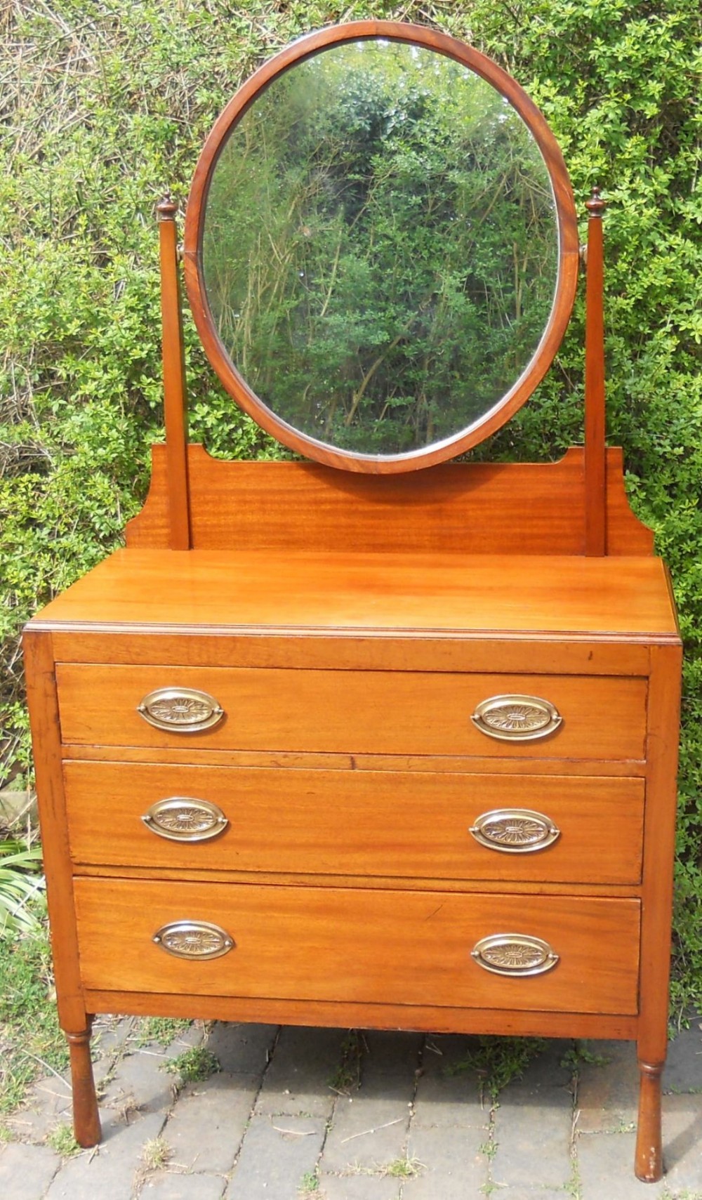 An Edwardian mahogany dressing table featuring three drawers with oval brass handles and a swivel oval mirror mounted on top.