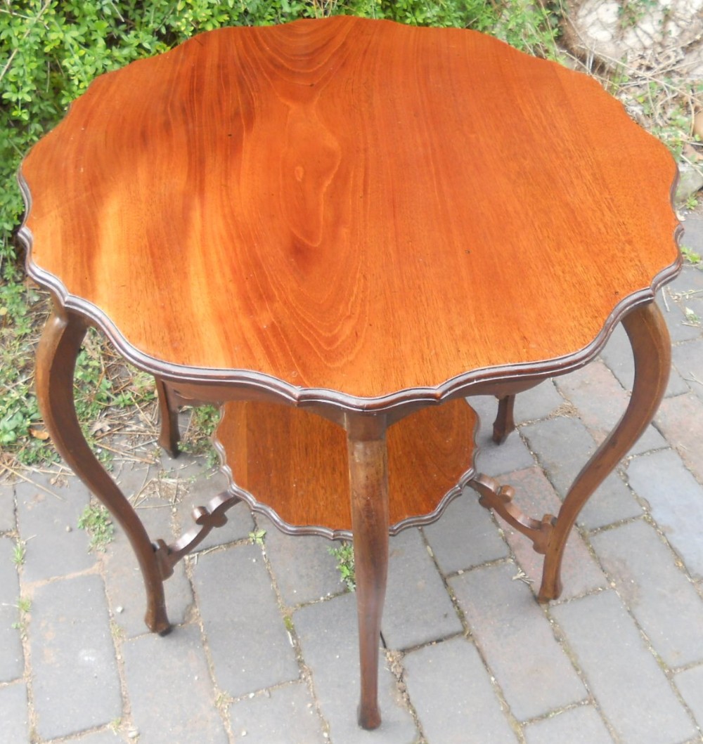 An Edwardian mahogany centre table featuring a scalloped shaped top, four slender cabriole legs, and a matching shaped lower undertier.