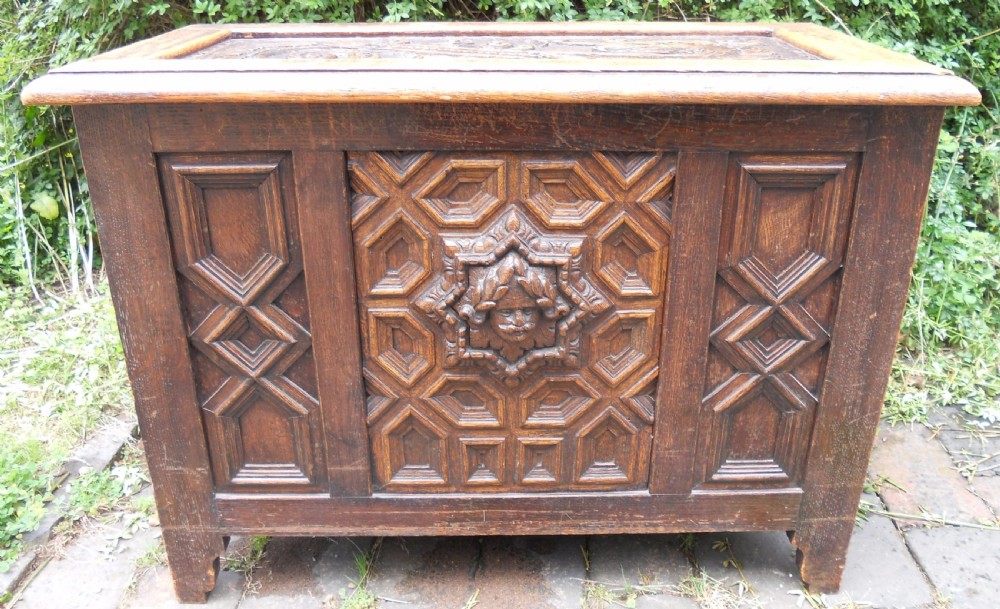 A rectangular Victorian carved oak blanket chest featuring a central carved face mask surrounded by geometric panel mouldings.