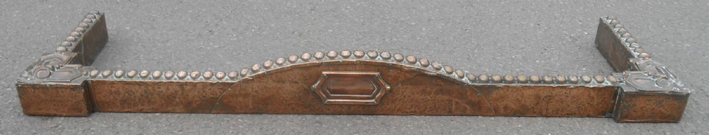 An Arts and Crafts copper fireside kerb featuring a raised arched centre, decorative studding along the upper edge, and ornate corner brackets.