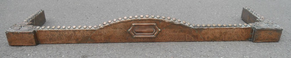 An Arts and Crafts copper fireside kerb featuring a raised arched centre, decorative studding along the upper edge, and ornate corner brackets. View II