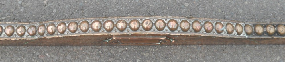 An Arts and Crafts copper fireside kerb featuring a raised arched centre, decorative studding along the upper edge, and ornate corner brackets. View IV