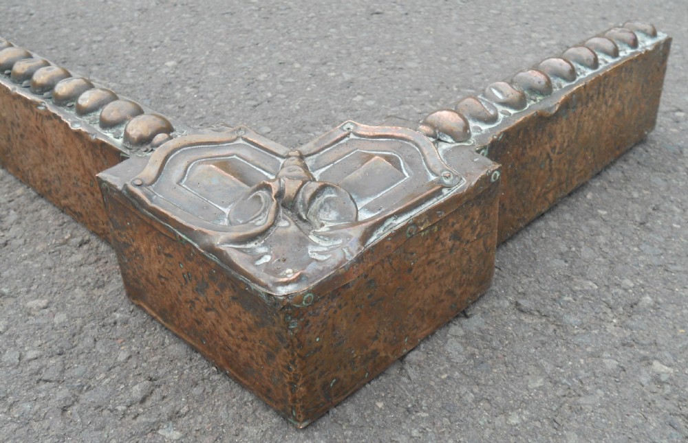 An Arts and Crafts copper fireside kerb featuring a raised arched centre, decorative studding along the upper edge, and ornate corner brackets. View VI