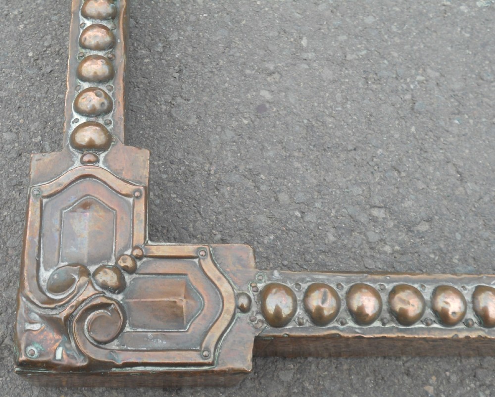 An Arts and Crafts copper fireside kerb featuring a raised arched centre, decorative studding along the upper edge, and ornate corner brackets. View VIII