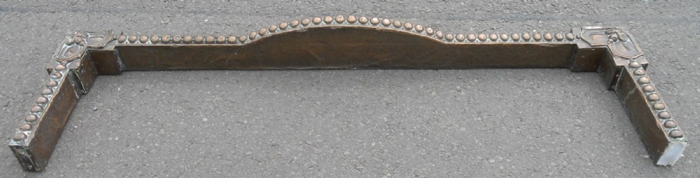 An Arts and Crafts copper fireside kerb featuring a raised arched centre, decorative studding along the upper edge, and ornate corner brackets. View X