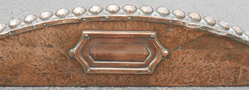An Arts and Crafts copper fireside kerb featuring a raised arched centre, decorative studding along the upper edge, and ornate corner brackets. View XI