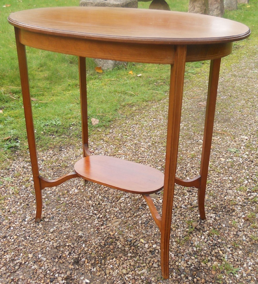 An Edwardian mahogany oval occasional table featuring splayed legs, line inlay around the top apron, and a lower oval undertier shelf.