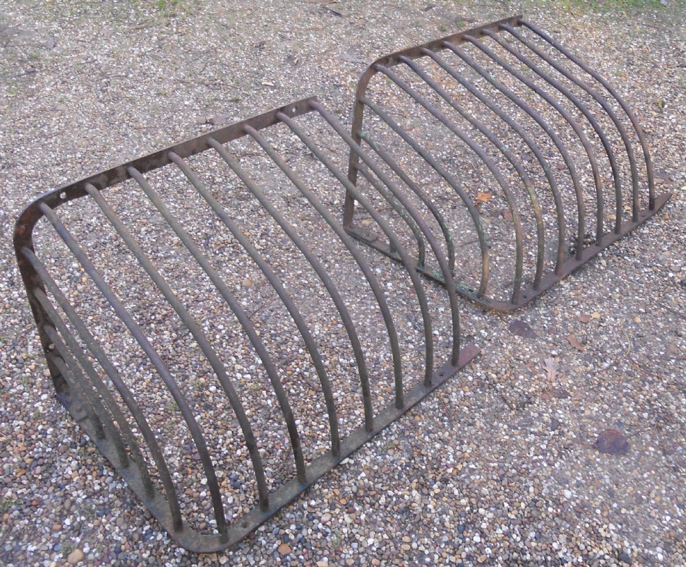 A pair of Victorian dark wrought iron curved hay racks featuring vertical metal bars and mounting plates.