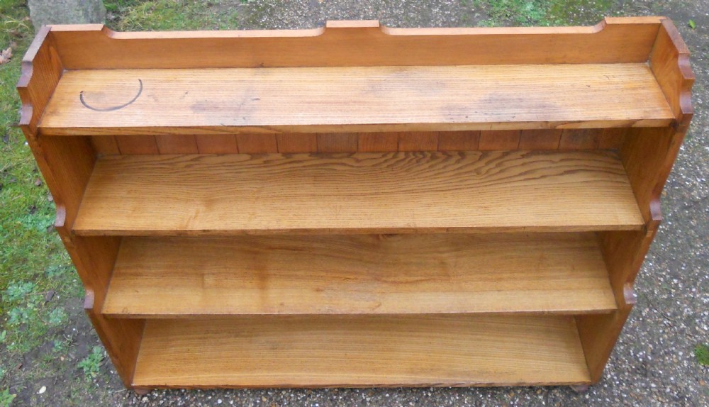 An Edwardian solid oak open waterfall bookcase featuring four tiers with stepped sides, a plank back, and a shaped top gallery. View X