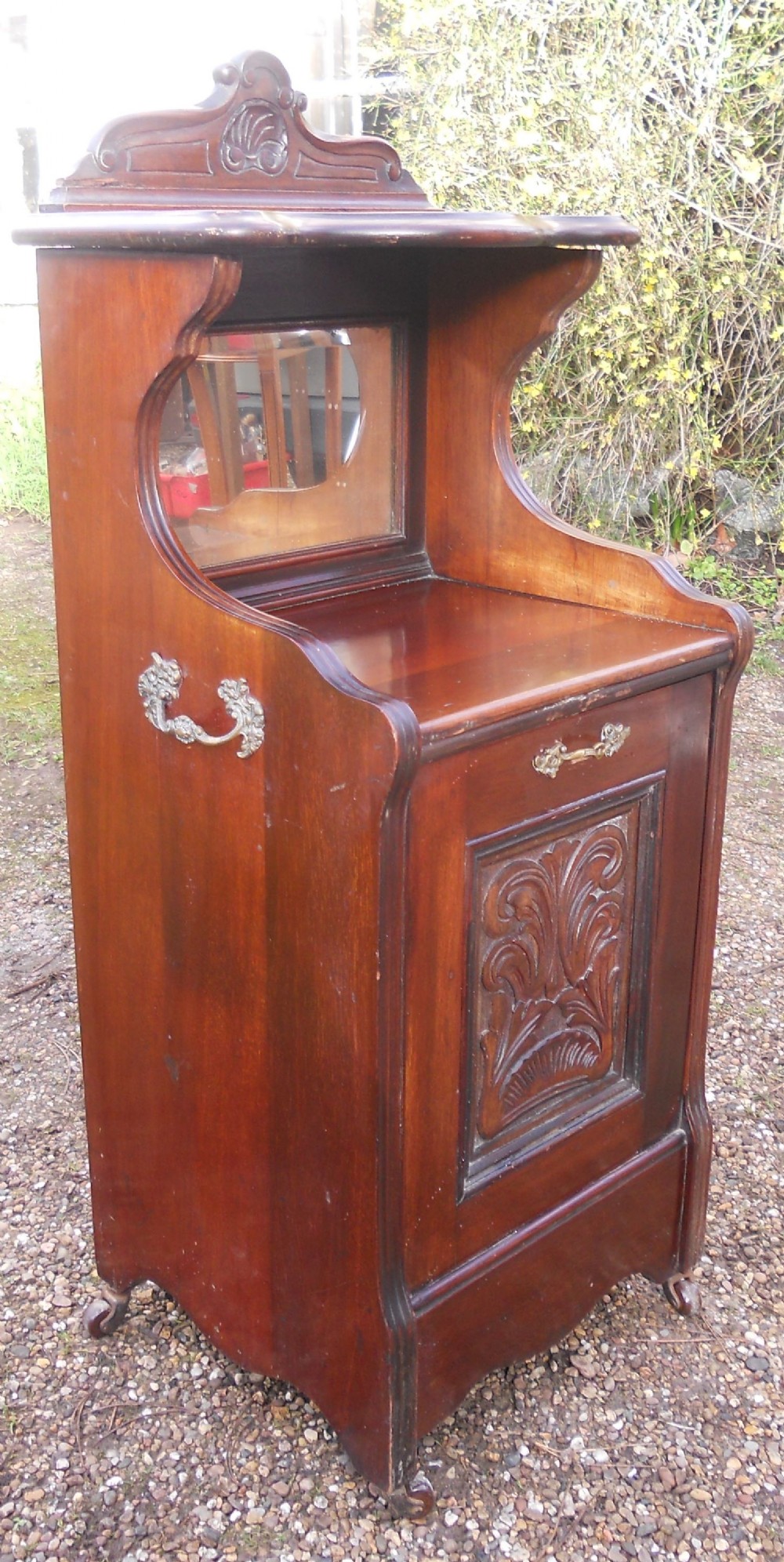 An Edwardian mahogany coal purdonium with an upper shelf featuring a mirror back, a carved fall-front door, and side metal handles.