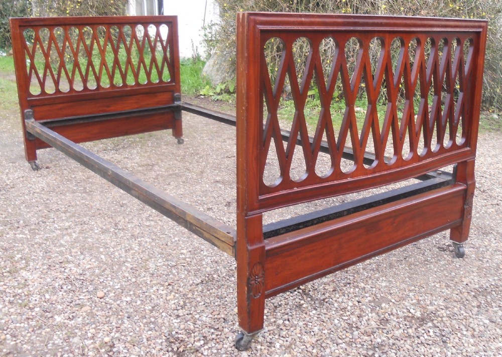An Edwardian mahogany single bed frame featuring a lattice fretwork headboard and footboard on brass castors.