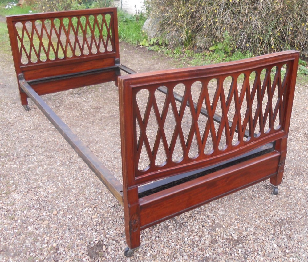 An Edwardian mahogany single bed frame featuring a lattice fretwork headboard and footboard on brass castors. View II