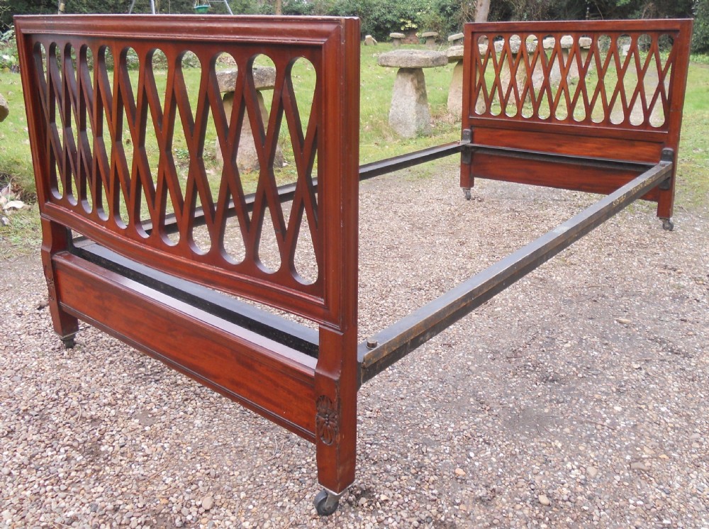 An Edwardian mahogany single bed frame featuring a lattice fretwork headboard and footboard on brass castors. View V
