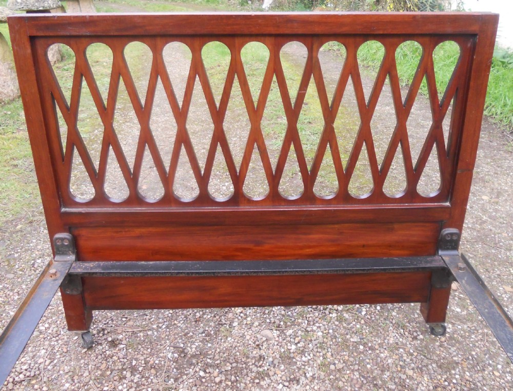 An Edwardian mahogany single bed frame featuring a lattice fretwork headboard and footboard on brass castors. View VI