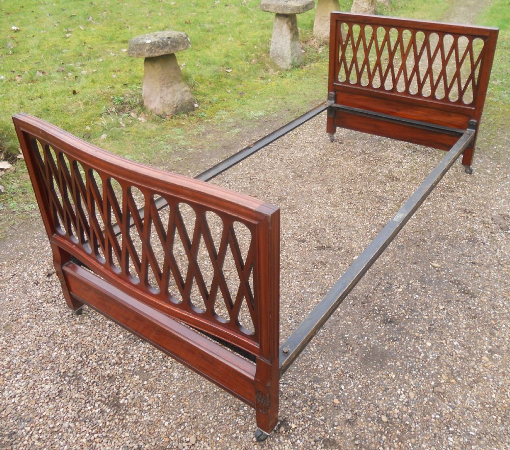 An Edwardian mahogany single bed frame featuring a lattice fretwork headboard and footboard on brass castors. View VII