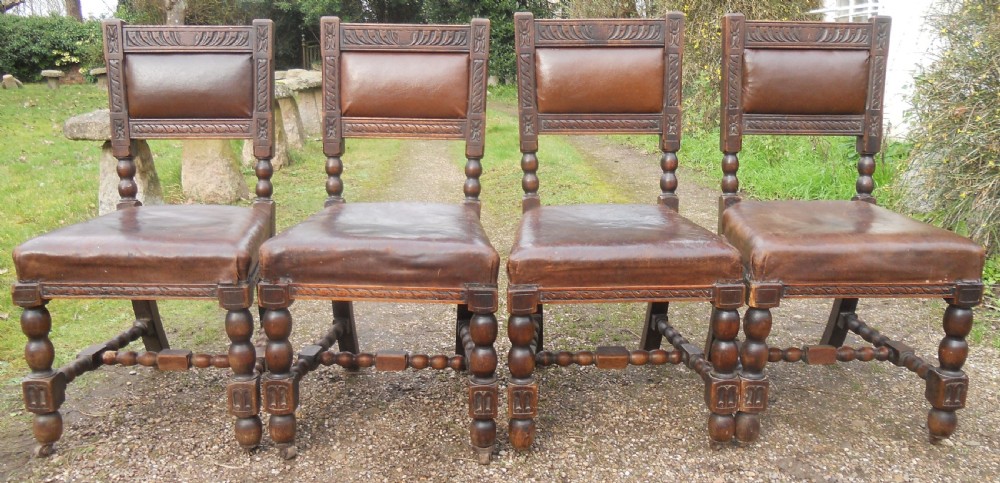 A set of four antique dark oak dining chairs featuring carved backrests, turned legs, and brown leather upholstered seats.