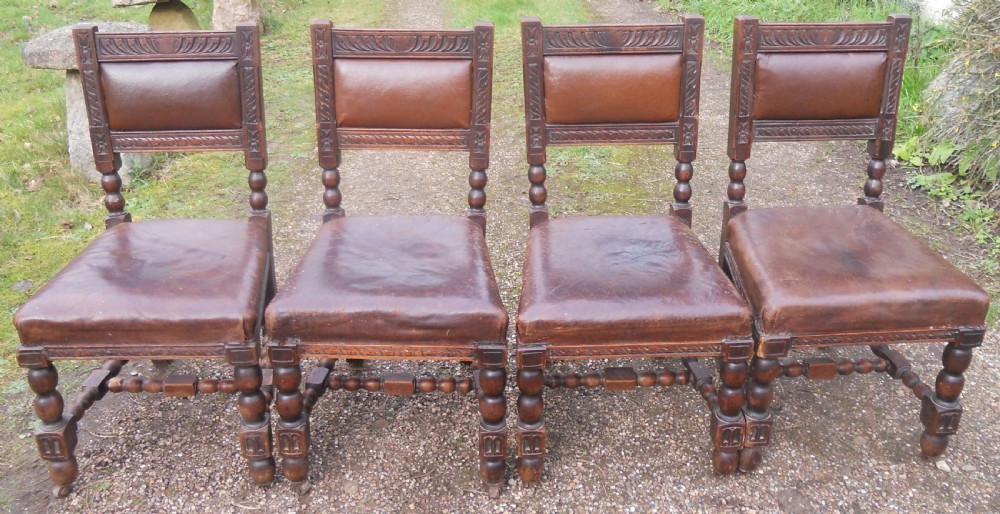 A set of four antique dark oak dining chairs featuring carved backrests, turned legs, and brown leather upholstered seats. View II